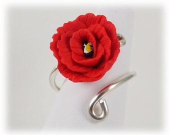 Può includere: Un anello d'argento con un fiore di papavero rosso fatto di pasta polimerica. Il fiore ha un centro giallo.