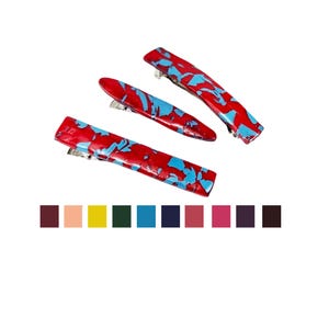 May include: Three red and blue patterned hair clips with silver metal clasps. The clips are arranged on a white background. A color palette of various shades is displayed below the clips.