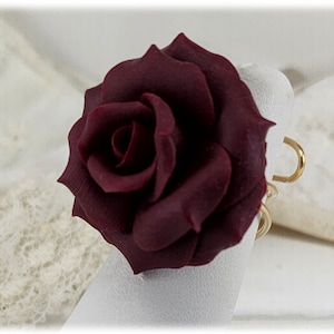 May include: A deep burgundy rose ring with a gold band. The rose is made of polymer clay and has a realistic appearance.