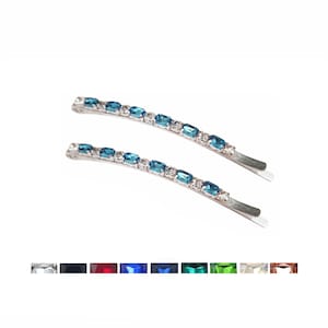 May include: Two silver-toned hair pins featuring a row of rectangular blue crystals interspersed with small clear stones. Below the pins, a horizontal colour palette displays ten distinct square crystal options in various shades including clear, black, red, blue, green, and pink.