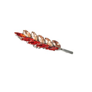 May include: A silver hair clip with a row of red and peach-colored rhinestones in a leaf shape.