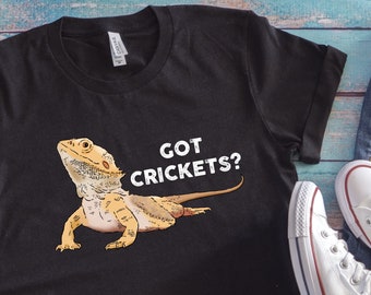 Op de afbeelding: Zwart T-shirt met een witte afbeelding van een baardagame en de tekst "GOT CRICKETS?"