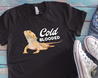 Op de afbeelding: Zwart T-shirt met een getekende baardagame en de tekst "Cold Blooded" in wit.