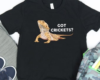 Può includere: Maglietta nera con un'immagine di un drago barbuto in stile cartone animato e il testo "GOT CRICKETS?"