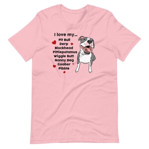 Op de afbeelding: Roze T-shirt met een cartoon afbeelding van een pit bull en de tekst "Ik hou van mijn... Pit Bull Derp Blockhead Pittiepotamus Wiggle Butt Nanny Dog Goober Pibble".