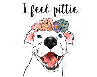May include: A white pit bull terrier with blue eyes wearing a flower crown with pink, orange, purple, and green flowers. The dog is smiling and the text "I feel pittie" is above the dog.