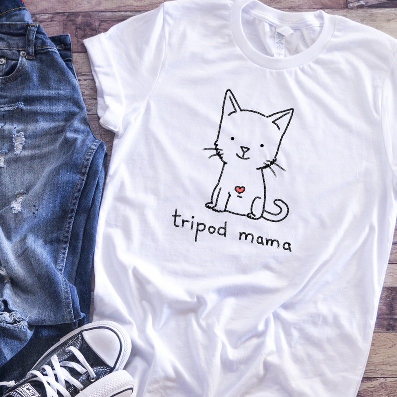 May include: White t-shirt with a black and white illustration of a cat with a red heart on its chest. The text "tripod mama" is printed below the cat.