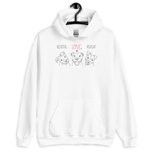 May include: White hoodie with a black line drawing of three dogs and the text "RESCUE LOVE REPEAT" in black with a red heart above the word "LOVE".