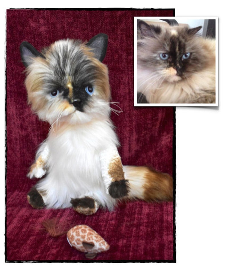 May include: A plush toy cat with a white, black, and brown coat, sitting on a red velvet surface. The toy cat has blue eyes and a serious expression. A small toy mouse is in front of the cat. A photo of a real cat is in the upper right corner of the image.