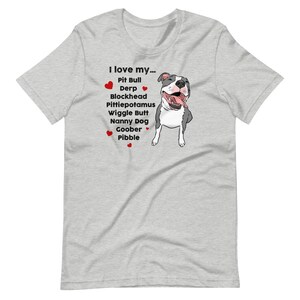 Op de afbeelding: Een grijs T-shirt met een afbeelding van een witte pit bull en de tekst "Ik hou van mijn... Pit Bull Derp Blockhead Pittiepotamus Wiggle Butt Nanny Dog Goober Pibble".