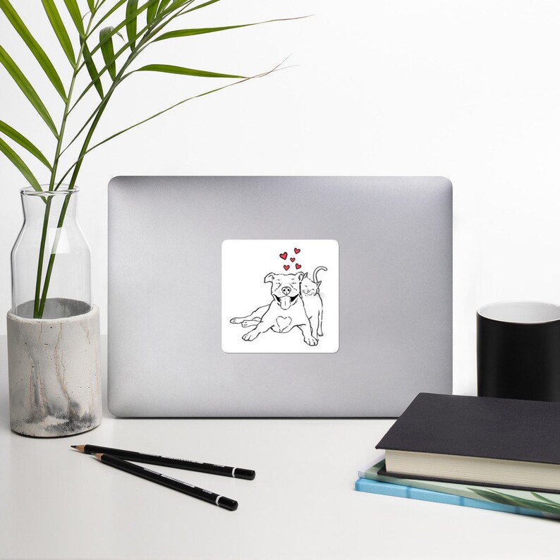 Puede incluir: Una pegatina cuadrada con una ilustraci&oacute;n en blanco y negro de un perro y un gato. El perro est&aacute; tumbado con un coraz&oacute;n en el pecho, y el gato est&aacute; a su lado. Varios corazones rojos flotan sobre ellos.