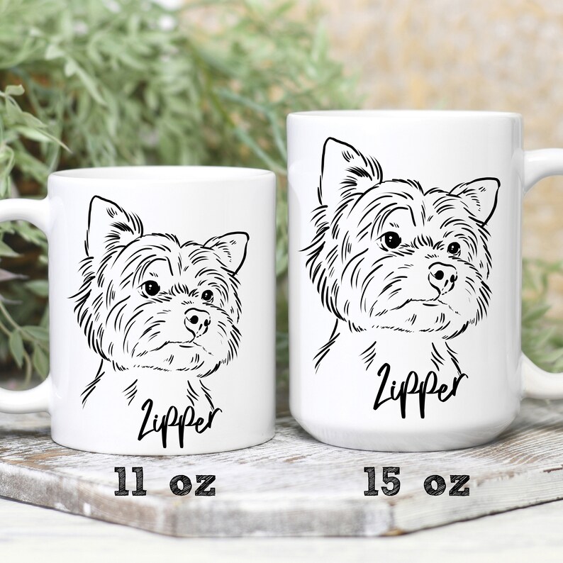 May include: Two white ceramic mugs with a black line drawing of a Yorkshire Terrier. The smaller mug is 11 oz and the larger mug is 15 oz. Both mugs have the name "Zipper" printed below the dog.