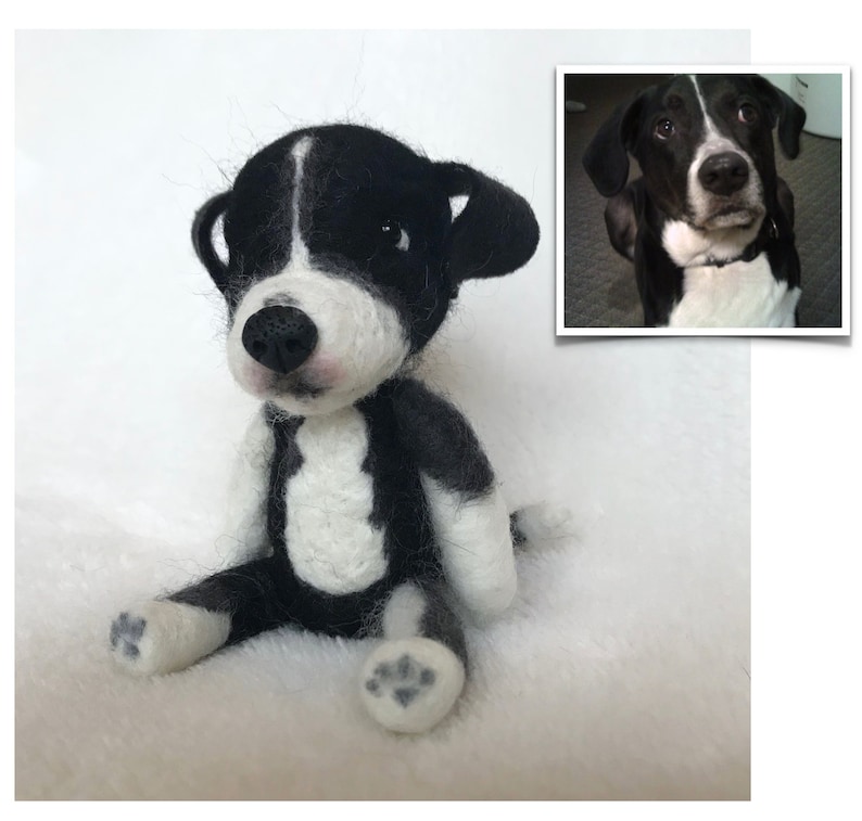 Op de afbeelding: Een zwart-wit naaldgevoelde hondenspeelgoed, zittend op een wit, pluche oppervlak. Het speelgoed is een replica van een echte hond, met een zwart-witte vacht, een roze neus en zwarte ogen.