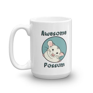 Puede incluir: Taza de cer&aacute;mica blanca con un c&iacute;rculo azul y un opossum de dibujos animados asom&aacute;ndose. El texto "Awesome Possum" est&aacute; impreso en la taza.