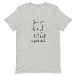 May include: A gray t-shirt with a black and white illustration of a cat with a red heart on its chest. The text "tripod dad" is printed below the cat.