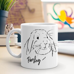 May include: White ceramic mug with a black line drawing of a rabbit with floppy ears and the name "Parsley" written underneath.