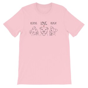 Puede incluir: Camiseta rosa con un dibujo en l&iacute;nea negra de tres perros y el texto "RESCUE LOVE REPEAT" con un coraz&oacute;n rojo sobre la palabra "LOVE".
