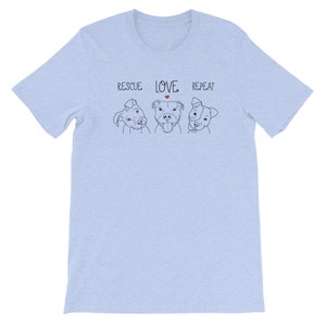 Puede incluir: Camiseta azul claro con un gr&aacute;fico de tres perros y el texto "RESCUE LOVE REPEAT" con un peque&ntilde;o coraz&oacute;n rojo sobre la palabra "LOVE".