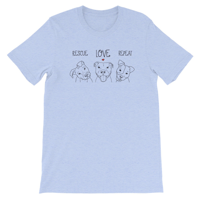 Puede incluir: Camiseta azul claro con un gr&aacute;fico de tres perros y el texto "RESCUE LOVE REPEAT" con un peque&ntilde;o coraz&oacute;n rojo sobre la palabra "LOVE".