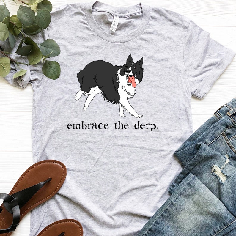 May include: A grey t-shirt featuring a black and white illustration of a border collie dog with its tongue out. The text "embrace the derp." is printed below the dog.