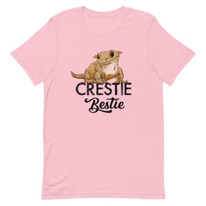 May include: Pink t-shirt with a cartoon crested gecko and the text "Crestiebestie".