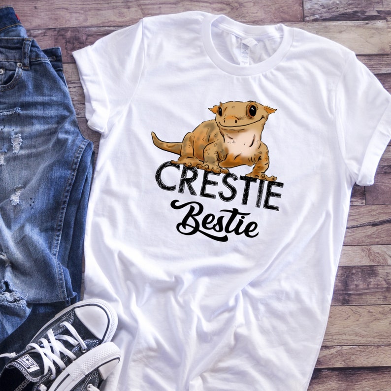 May include: White t-shirt with a cartoon crested gecko and the text "Crestiebestie" in black.