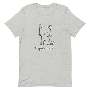 May include: A gray t-shirt with a black and white illustration of a cat with a red heart on its chest. The text "tripod mama" is printed below the cat.