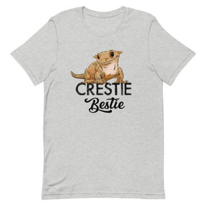 May include: A heather grey t-shirt with a cartoon crested gecko and the text "Crestiebestie" in black.