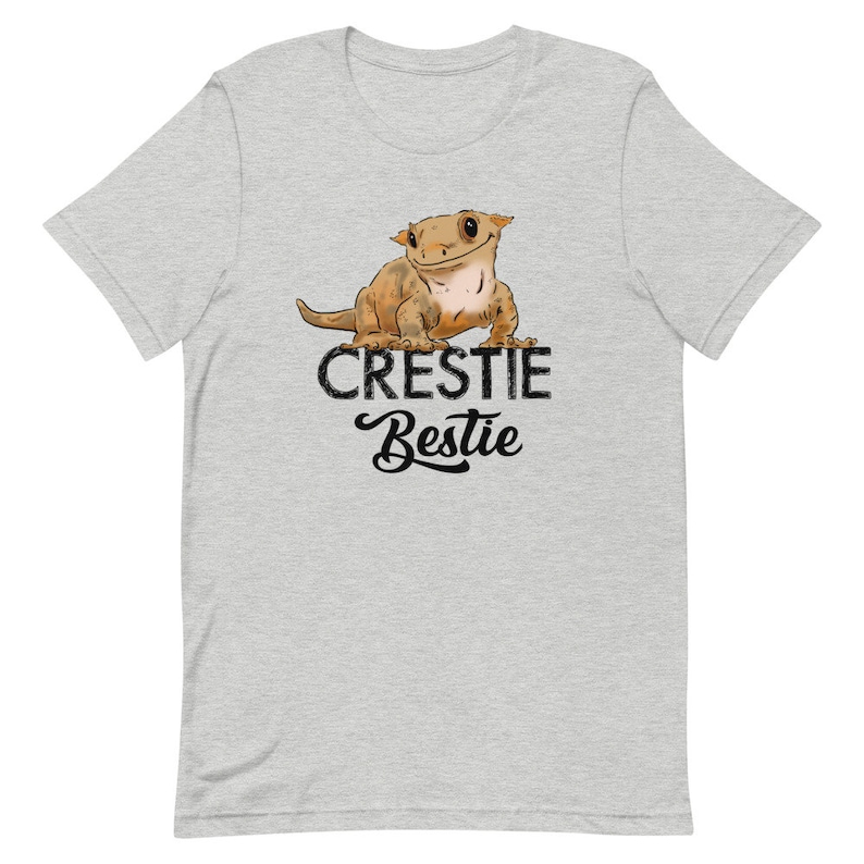 May include: A heather grey t-shirt with a cartoon crested gecko and the text "Crestiebestie" in black.