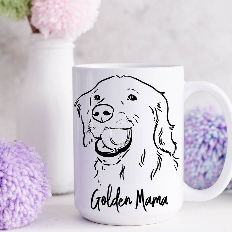 May include: White ceramic mug with a black line drawing of a Golden Retriever dog with its mouth open and a ball in its mouth. The text "Golden Mama" is printed in black at the bottom of the mug.