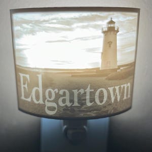 Może przedstawiać: Biała ceramiczna lampka nocna z obrazkiem latarni morskiej i tekstem "Edgartown".