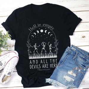 Puede incluir: Camiseta negra con un estampado gráfico blanco de tres esqueletos bailando bajo una luna creciente con el texto "El infierno está vacío y todos los demonios están aquí" y "William Shakespeare" en la parte inferior.