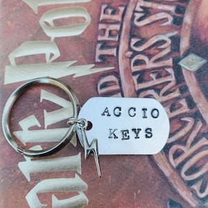 May include: A silver keychain with a lightning bolt charm and a tag that says "Accio Keys". The keychain is on top of a book with the title "Harry Potter and the Sorcerer's Stone".