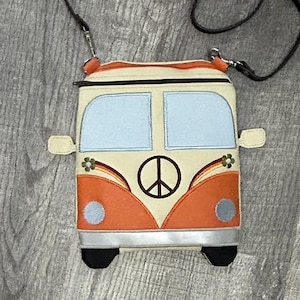May include: A cream, orange, and blue crossbody bag shaped like a vintage VW bus. The bag features a peace sign, rainbow accents, and black wheels. The bag has a black strap and a zip closure.