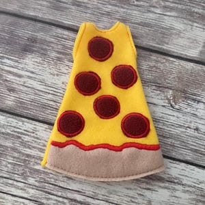 Puede incluir: Una porción de pizza de fieltro en amarillo con pepperoni rojo y una corteza marrón claro. La porción de pizza está diseñada para ser usada como disfraz o accesorio. El diseño es simple y colorido, perfecto para un look divertido con temática de comida.