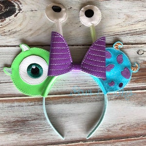 Könnte beinhalten: Stirnband mit lila Schleife und grünen und blauen Filzmonsterohren. Die Ohren haben große Augen und ein einzelnes Horn.