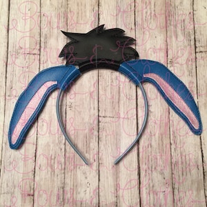 May include: A blue and pink headband with black ears and a black hairpiece. The headband is made of felt and is designed to look like a cartoon character.