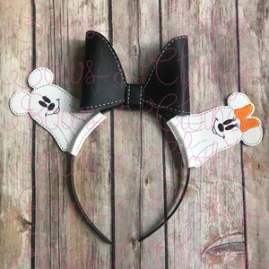 Könnte beinhalten: Ein schwarzes Schleifen-Haarband mit weißen Geisterohren. Die Ohren haben gestickte Mickey-Maus-Gesichter und ein Ohr hat eine orange Schleife.