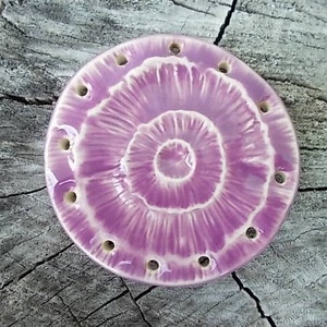 Könnte beinhalten: Eine runde Keramik-Schale mit einem pink-weißen Swirl-Design. Die Schale hat mehrere Löcher am Rand.
