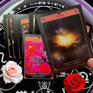 May include: A tarot card deck with black and red borders. One card reads "Wish" and another "Love". The "Wish" card shows a cosmic illustration. Two roses, one pink and one red, are also visible.
