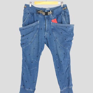 Può includere: Pantaloni in denim blu con vita a coulisse e più tasche. I pantaloni hanno un piccolo motivo nero ripetuto.