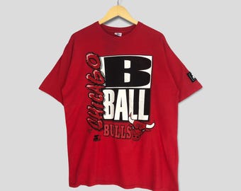 May include: Red short-sleeved t-shirt with a graphic print of the Chicago Bulls logo and the text "Chicago Ball Bulls".