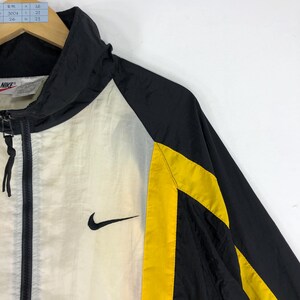 May include: Black and white windbreaker jacket with yellow accents and a Nike logo on the left side. The jacket has a zipper closure and a hood.