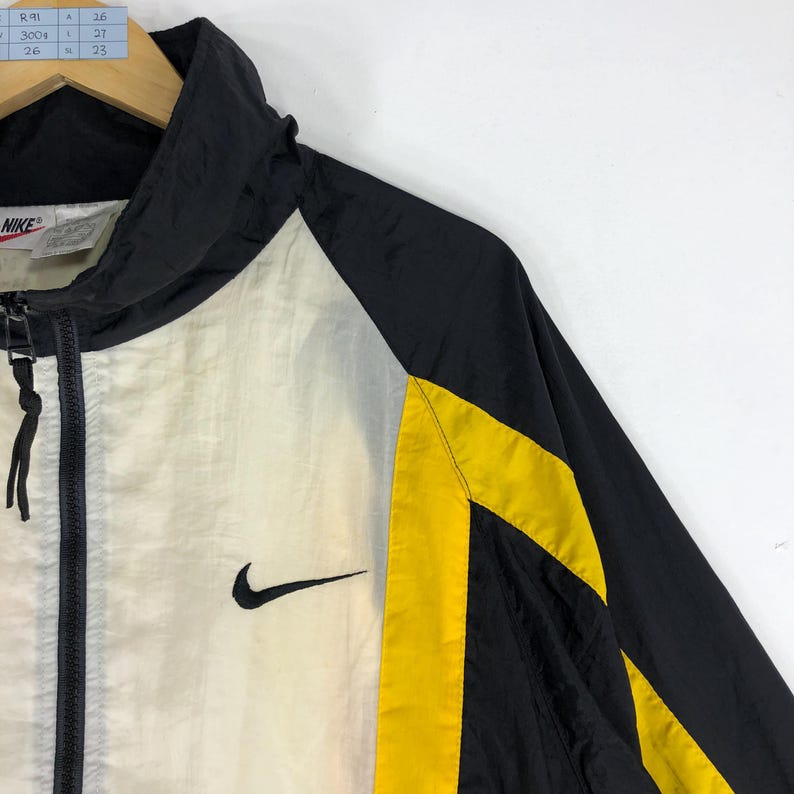 May include: Black and white windbreaker jacket with yellow accents and a Nike logo on the left side. The jacket has a zipper closure and a hood.