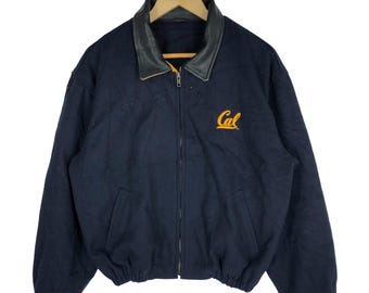 May include: Navy blue jacket with a black leather collar and a gold zipper. The jacket has the word "Cal" embroidered in gold on the chest. The jacket is hanging on a wooden hanger.