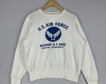 May include: A white crew neck sweatshirt featuring the text "U.S. AIR FORCE" in blue, a circular emblem, and the text "McGuire A.F. BASE NEW JERSEY". The sweatshirt has ribbed cuffs and hem.