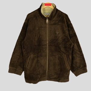 May include: A brown fleece zip-up jacket with a high collar and a zipper closure. The jacket has a speckled pattern and two pockets on the front.