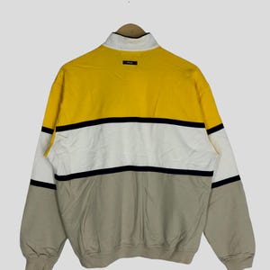 May include: A yellow, white and beige striped long-sleeved sweatshirt with a black zip and a small "P.L.A." logo on the back.
