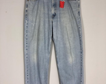 May include: Light blue denim jeans with a relaxed fit, hanging on a wooden hanger. The jeans have a classic five-pocket design, a button and zipper closure, and a red tag. The denim shows some wear and tear.