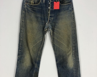 May include: A pair of blue denim jeans with a button fly and a red tag. The jeans are distressed and faded, with a worn look.